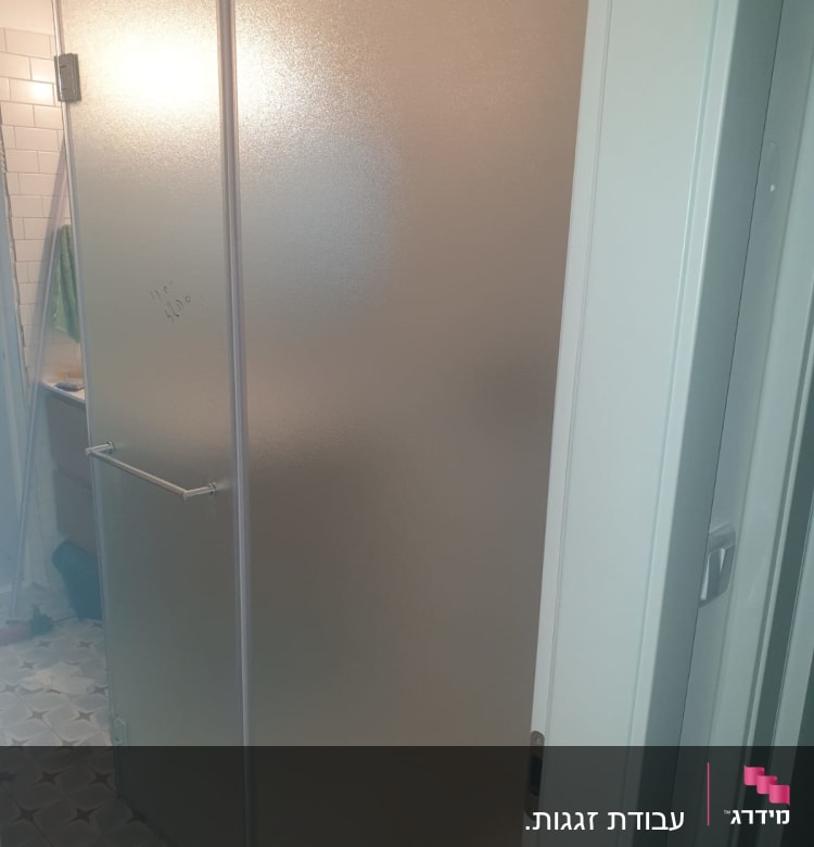 דלת זכוכית חלבית עם ידית מתכת בחדר אמבטיה